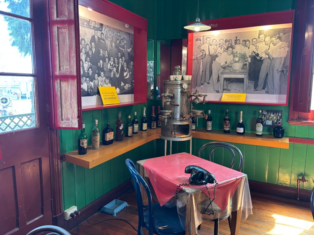 A cozy restaurant interior featuring a green and red color scheme, with vintage photographs on the walls, a wooden table covered with a pink tablecloth, a black phone, and various bottles of liquor displayed on a shelf.