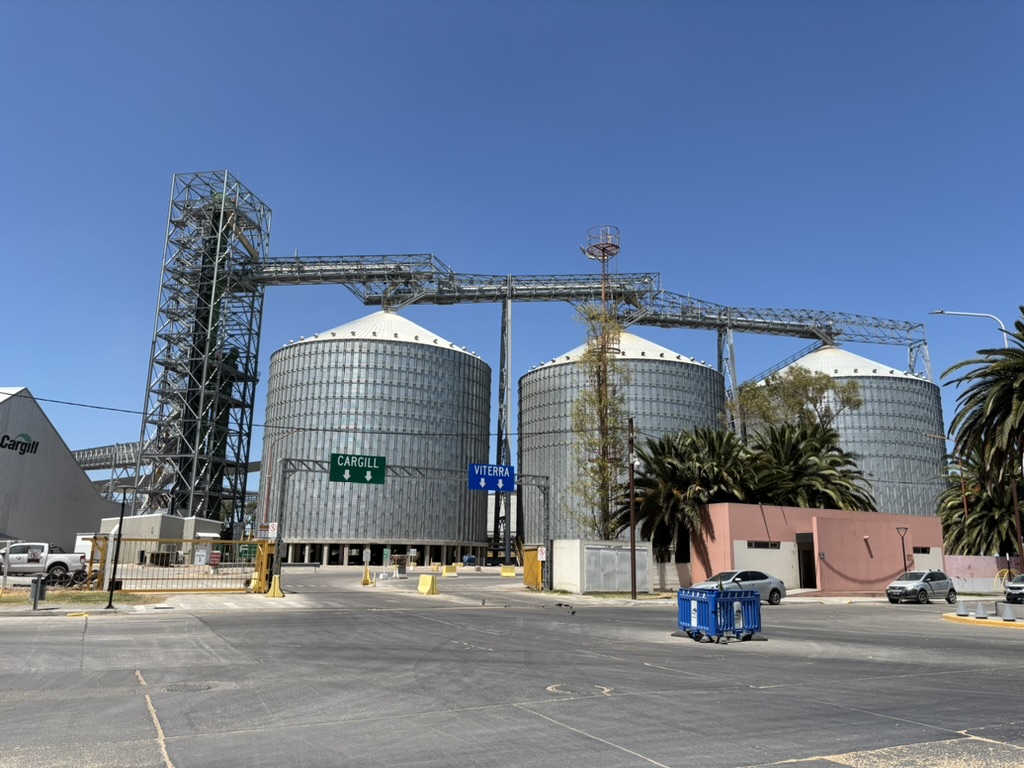 Large grain silos with metal structures in an industrial setting, featuring a Cargill sign and surrounding palm trees.