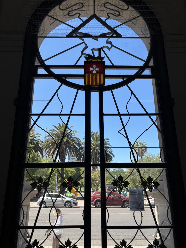 A decorative stained glass window featuring a central emblem and a view of palm trees and parked cars outside.