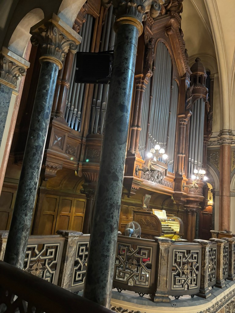 Interior view of a church organ with ornate wooden carvings, flanked by marble columns and a decorative railing.
