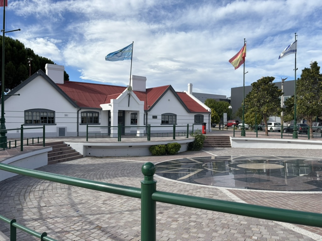 A building with a red roof surrounded by flags located in a public square with a decorative stone pavement.